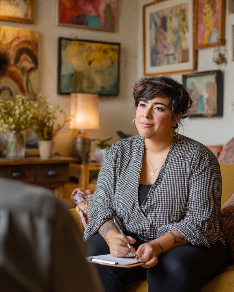 BIPOC therapist in a warm office with natural light, taking notes during a session